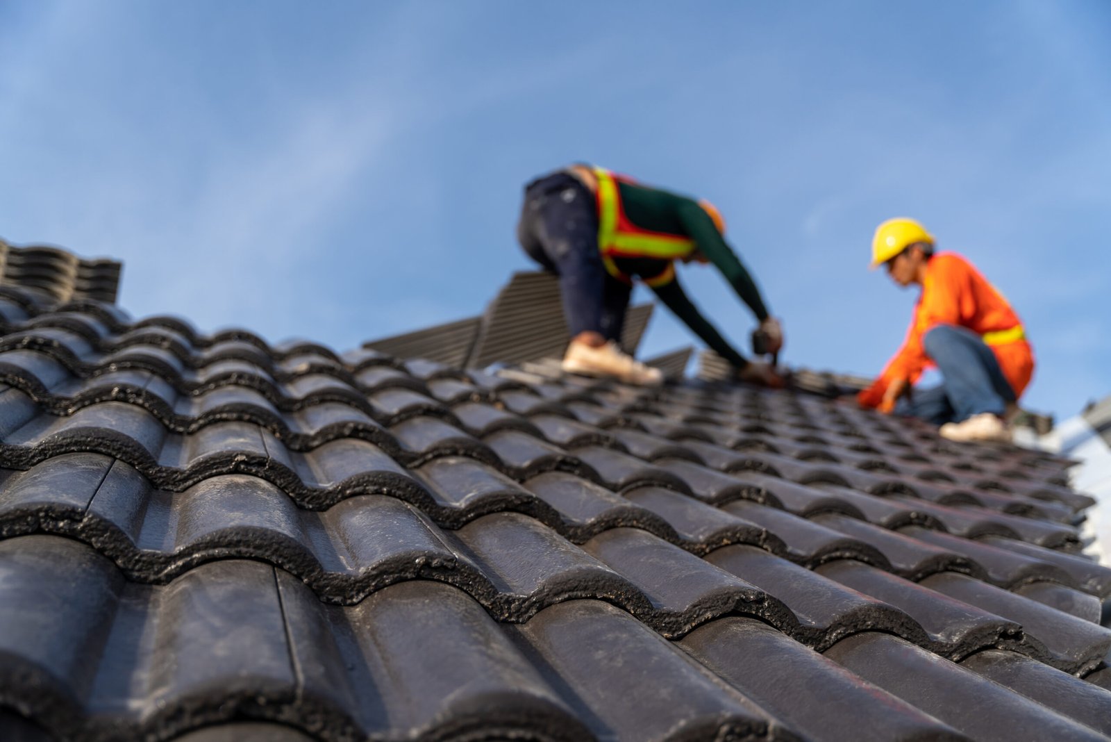 2 roofers working on the working at height to install the Concrete Roof Tiles on the new roof of new modern building construction. Selective focus of Concrete Roof Tiles.